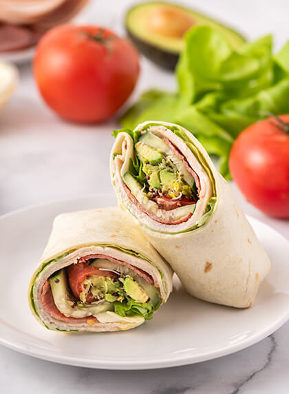 Freshly prepared wraps with avocado, tomato, and lettuce.
